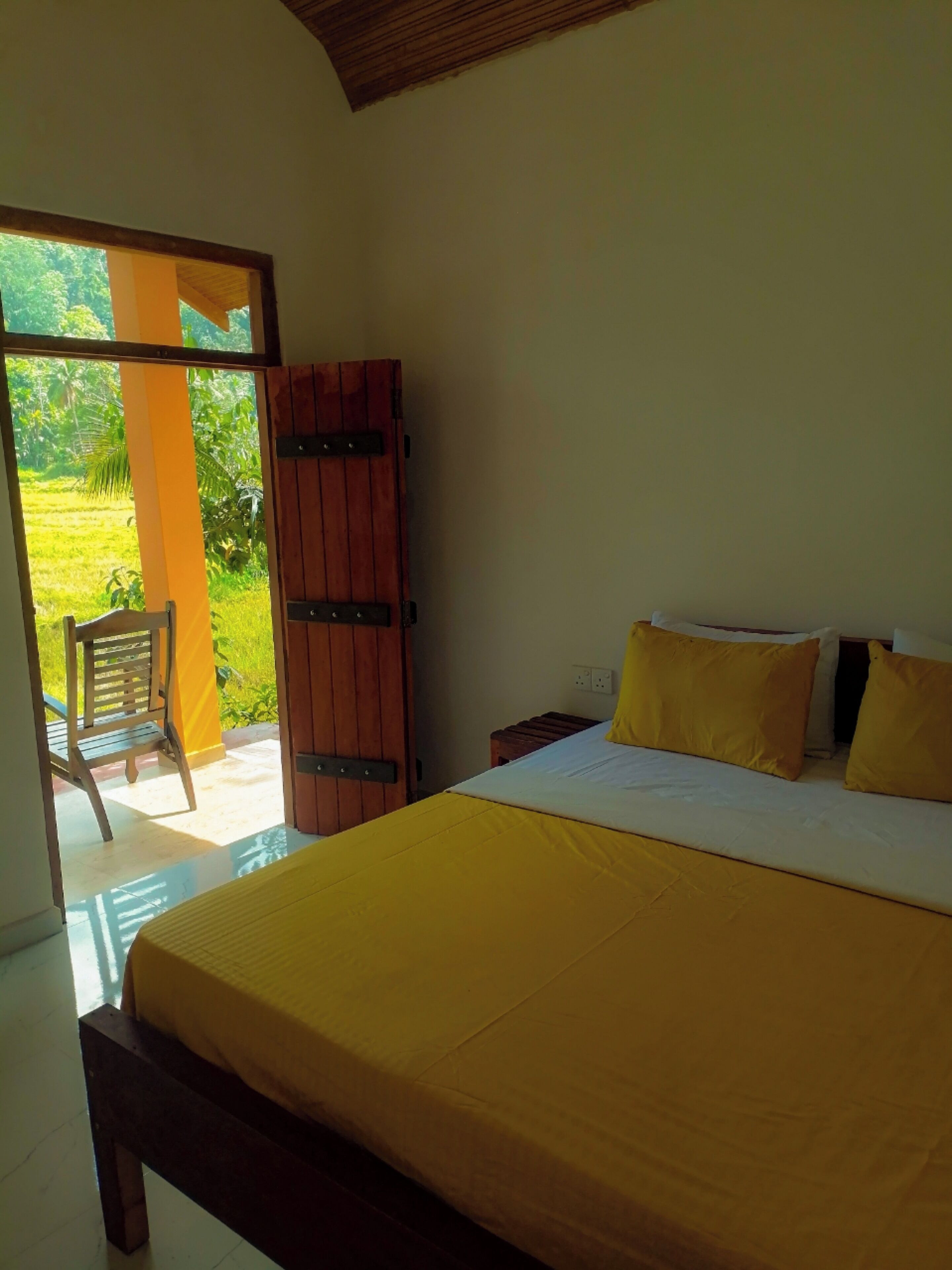 A bedroom with a bed, a wooden wardrobe, a chair, and a view of a green landscape through an open door.