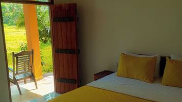A bedroom with a bed, a wooden wardrobe, a chair, and a view of a green landscape through an open door.