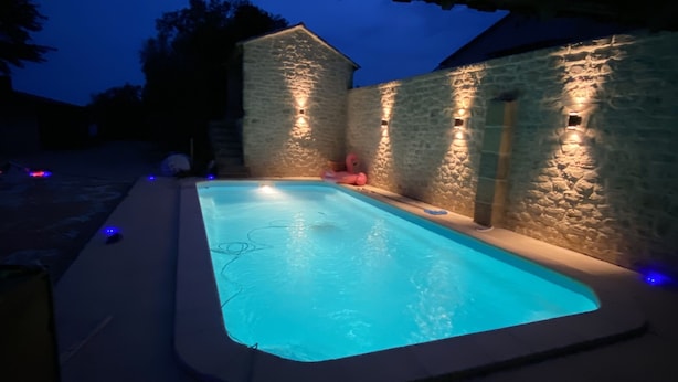 A swimming pool with a stone wall and a wooden pergola overhead.