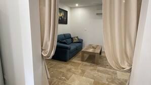 A living room with a blue sofa, a small wooden table, and beige curtains framing the space.