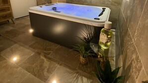 A modern bathroom with a large bathtub, stone tiles, and a small plant.