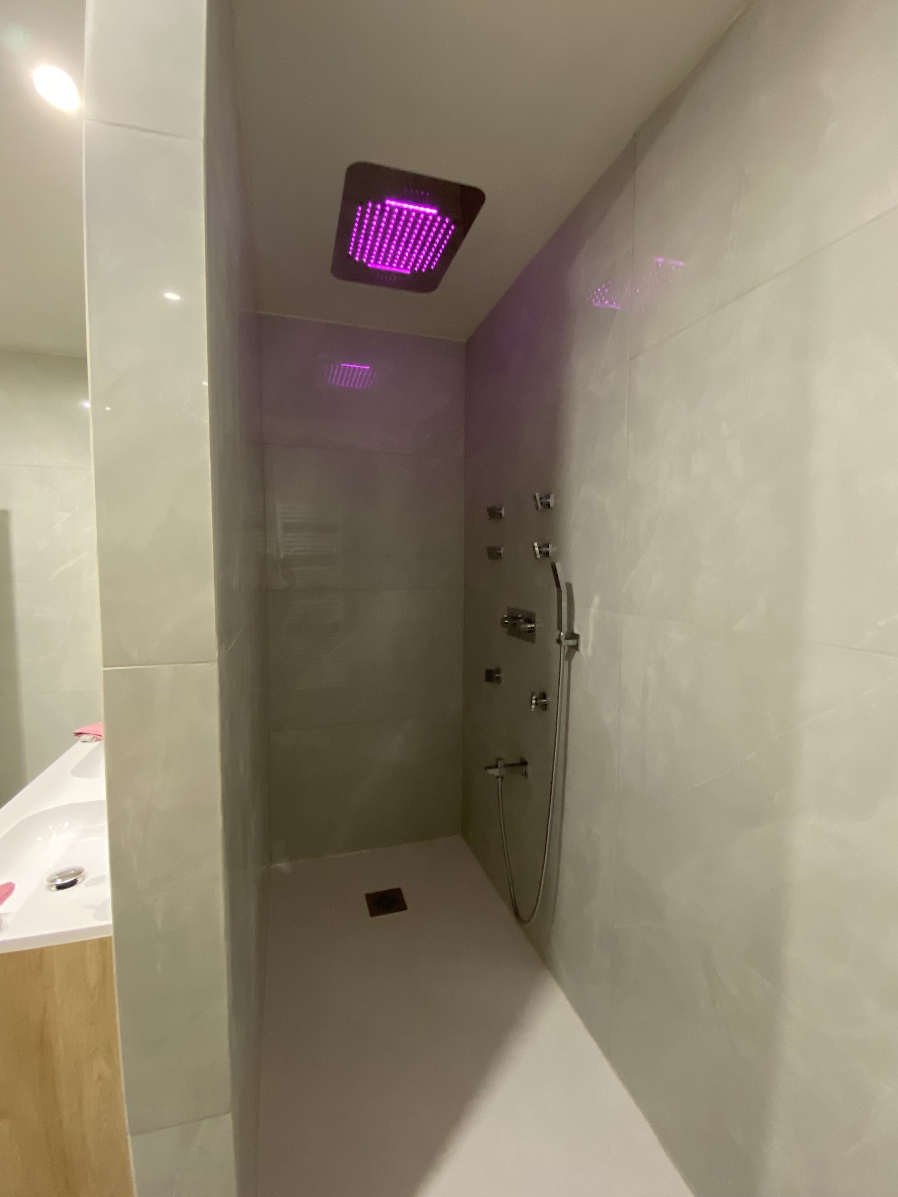 Un espace douche moderne doté d’un luminaire carré à LED et d’un pommeau de douche à main.