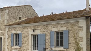 A stone building with blue shutters, a patio with a table and chairs, and a gravel driveway.
