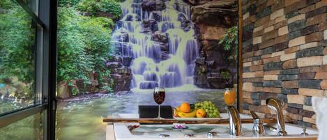 A bathroom with a waterfall mural, a wooden counter, and a fruit bowl.