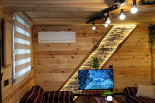 Interior acogedor de una cabaña de madera con televisión, una pared de piedra y un techo inclinado.