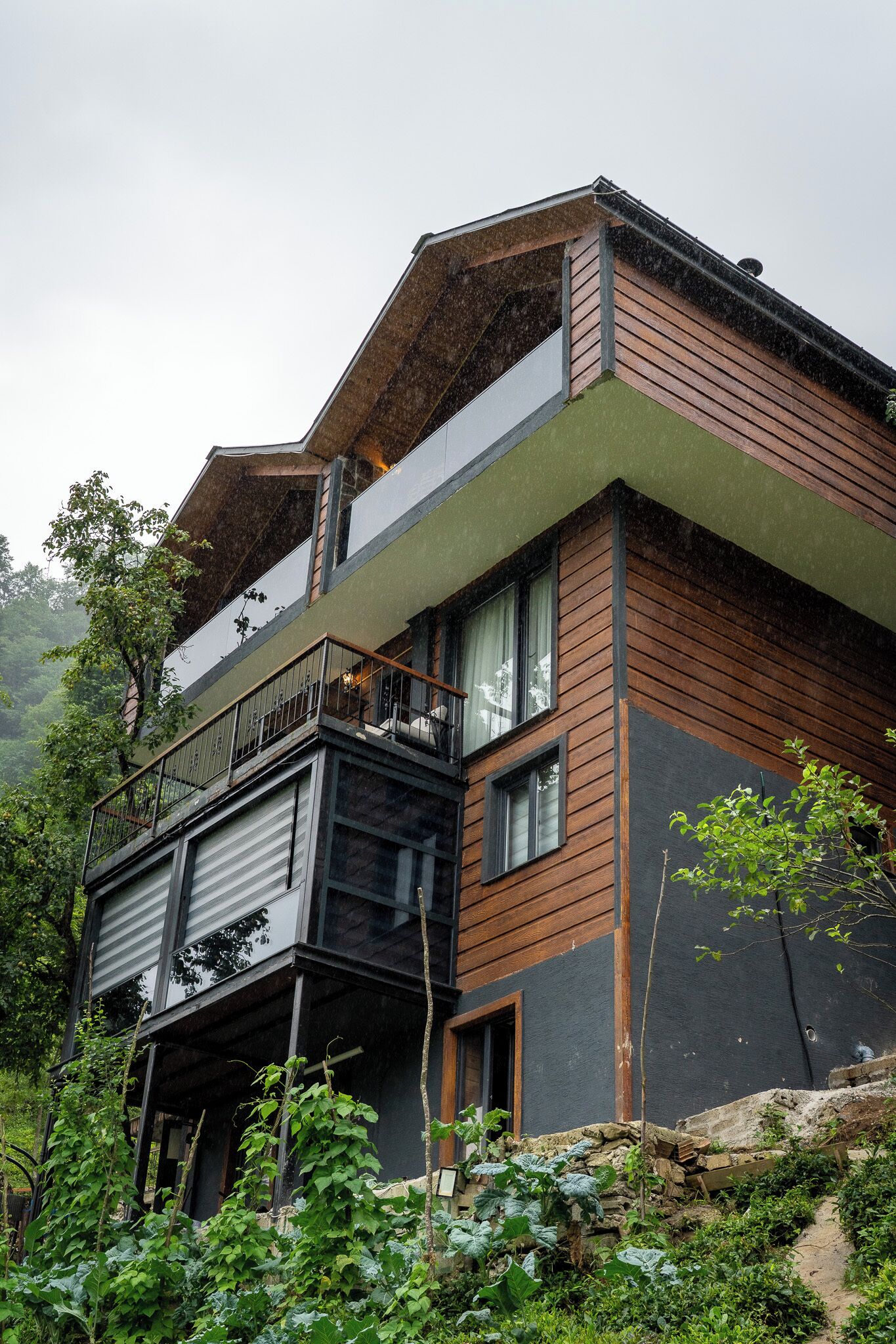 A modern two-story house with a balcony, surrounded by lush greenery.