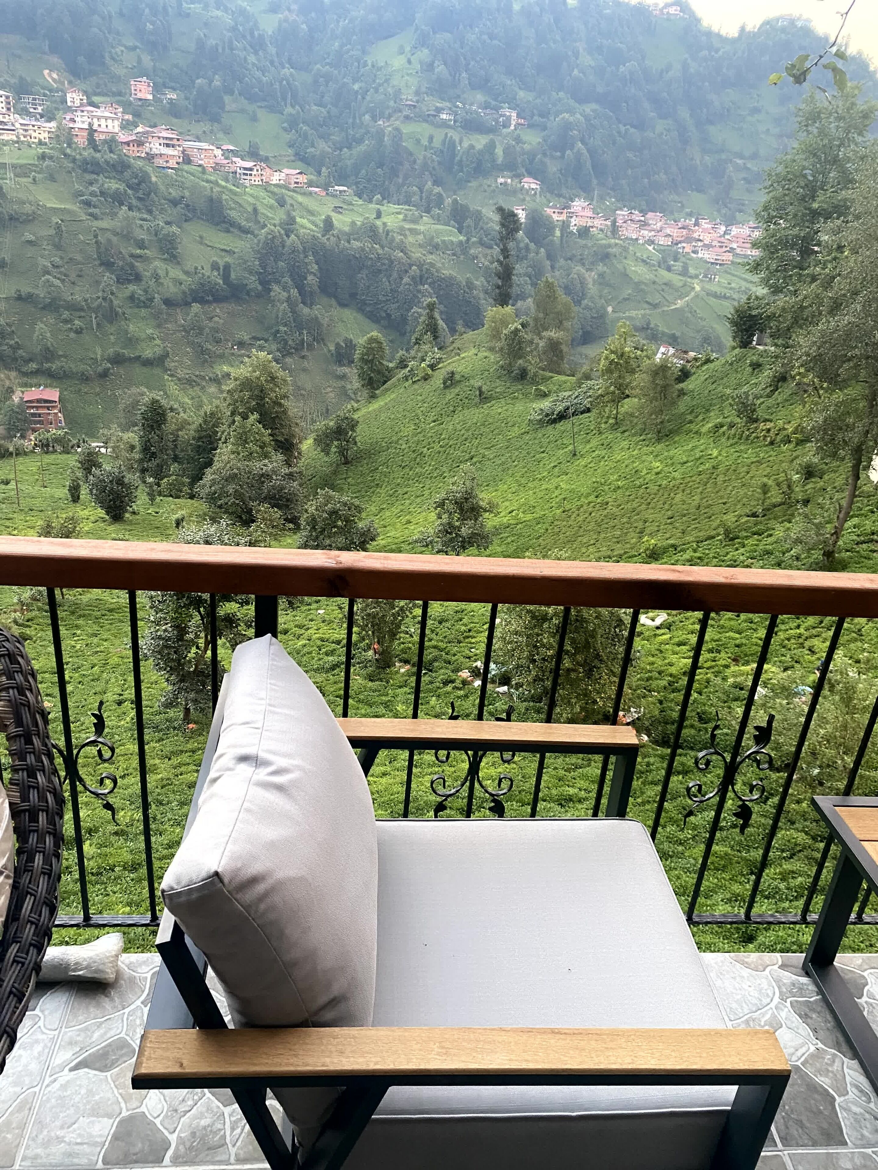 Un balcon agrémenté d’un fauteuil confortable et d’une table, offrant une vue sur un paysage verdoyant et luxuriant, avec des maisons à étages.