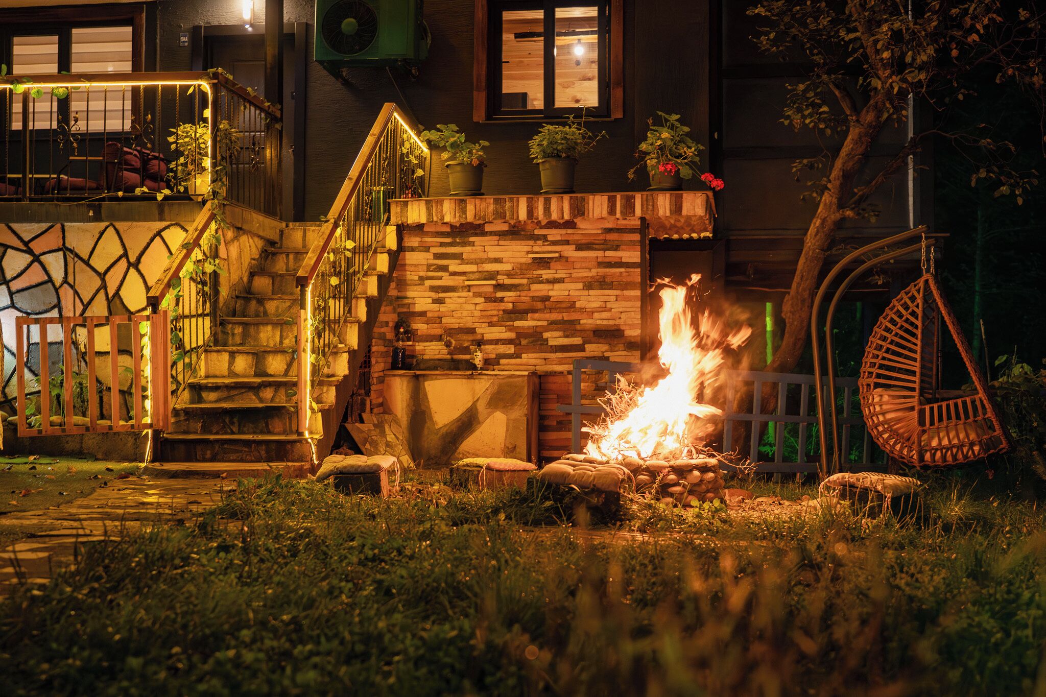 Een vuurkuil met een bakstenen muur en houten treden die leiden naar een balkon met planten.