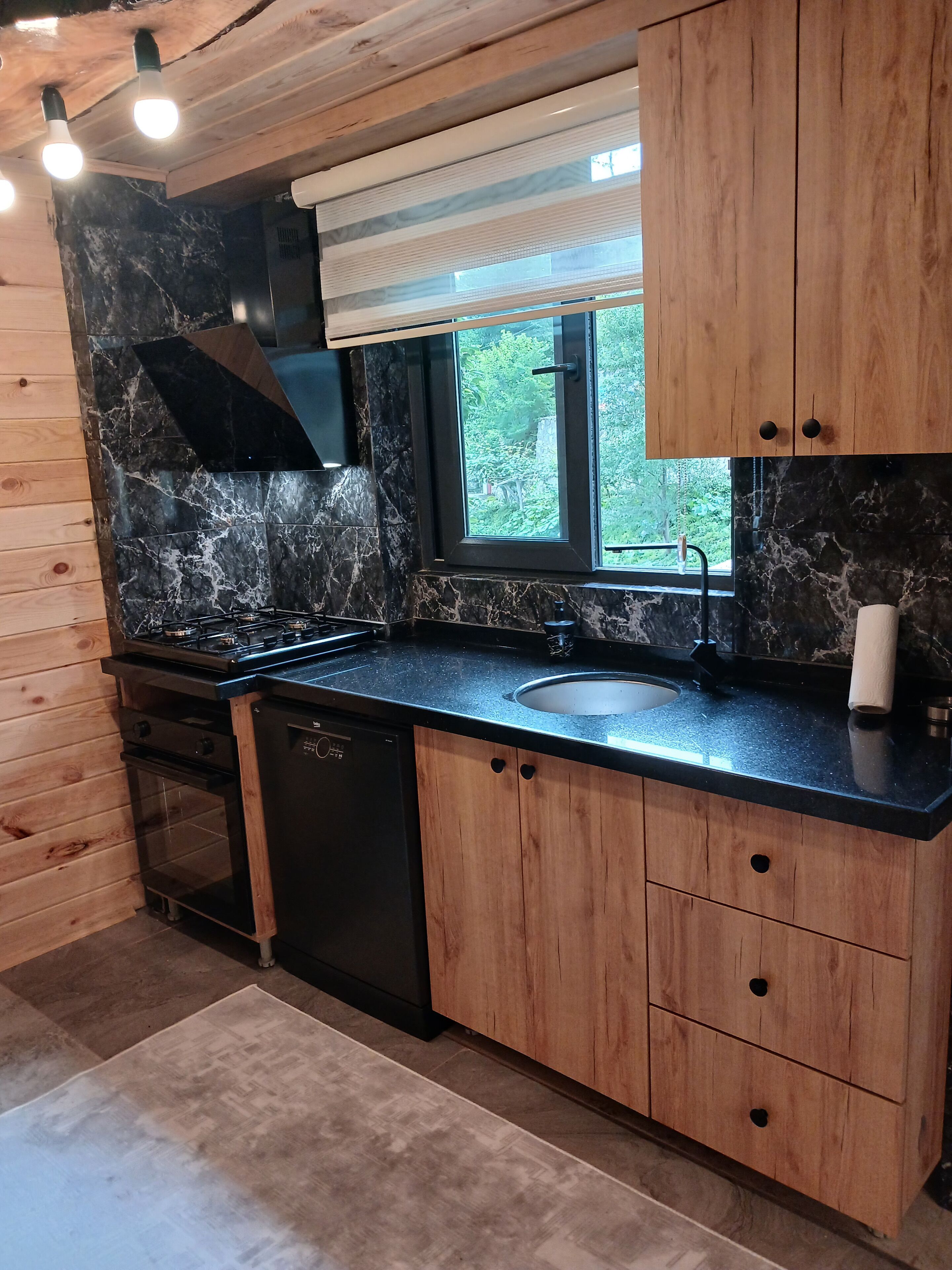 Una cocina moderna con salpicadero de mármol negro, armarios de madera y ventana con vistas a zonas verdes.