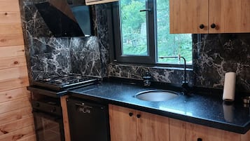 Una cocina moderna con salpicadero de mármol negro, armarios de madera y ventana con vistas a zonas verdes.