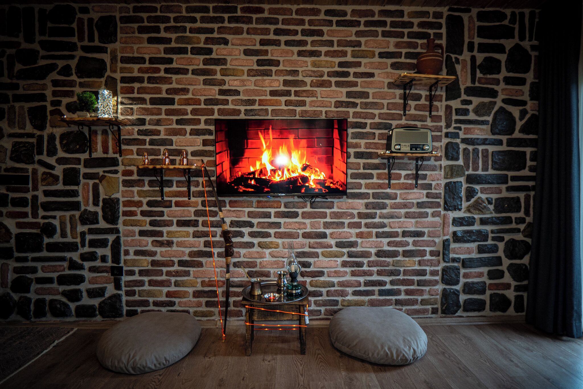 A room with a brick fireplace, a small table with a lamp, and two cushions on the floor.