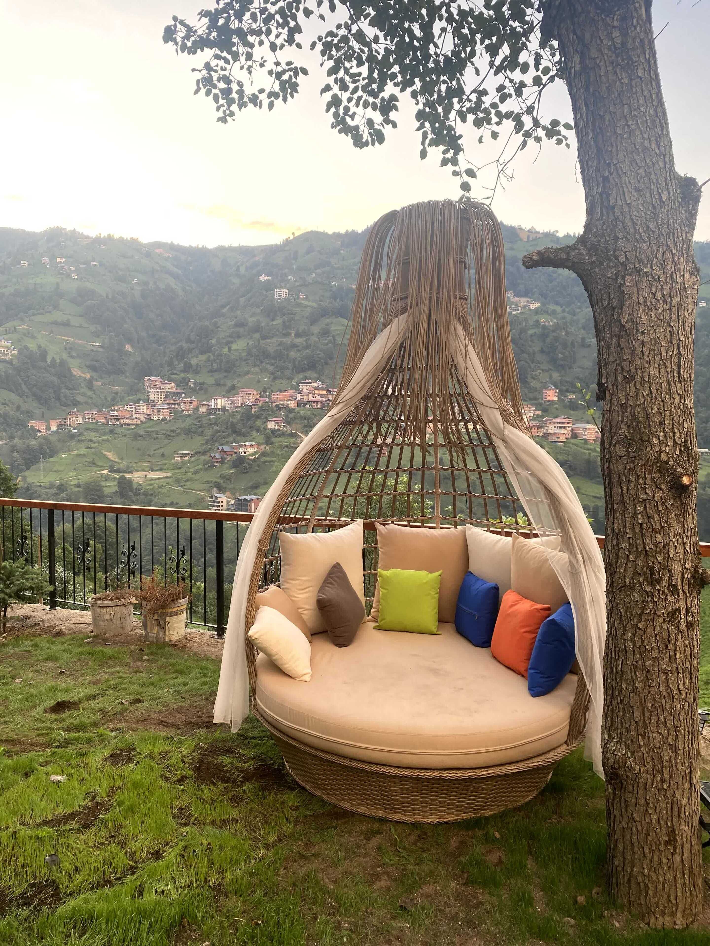 A hanging chair with cushions, a tree, and a view of a hillside with buildings.