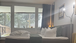 A bedroom with a bed, a sofa, a window with a view of trees, and a lamp. - Stressless Hotelapparat Inklusive Aktivcard Bayerischer Wald (Sankt Englmar)