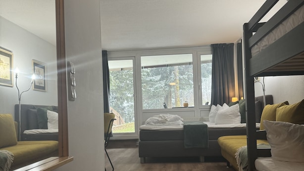 A room with bunk beds, a sofa, a desk, and a large window. - Stressless Hotelapparat Inklusive Aktivcard Bayerischer Wald (Sankt Englmar)