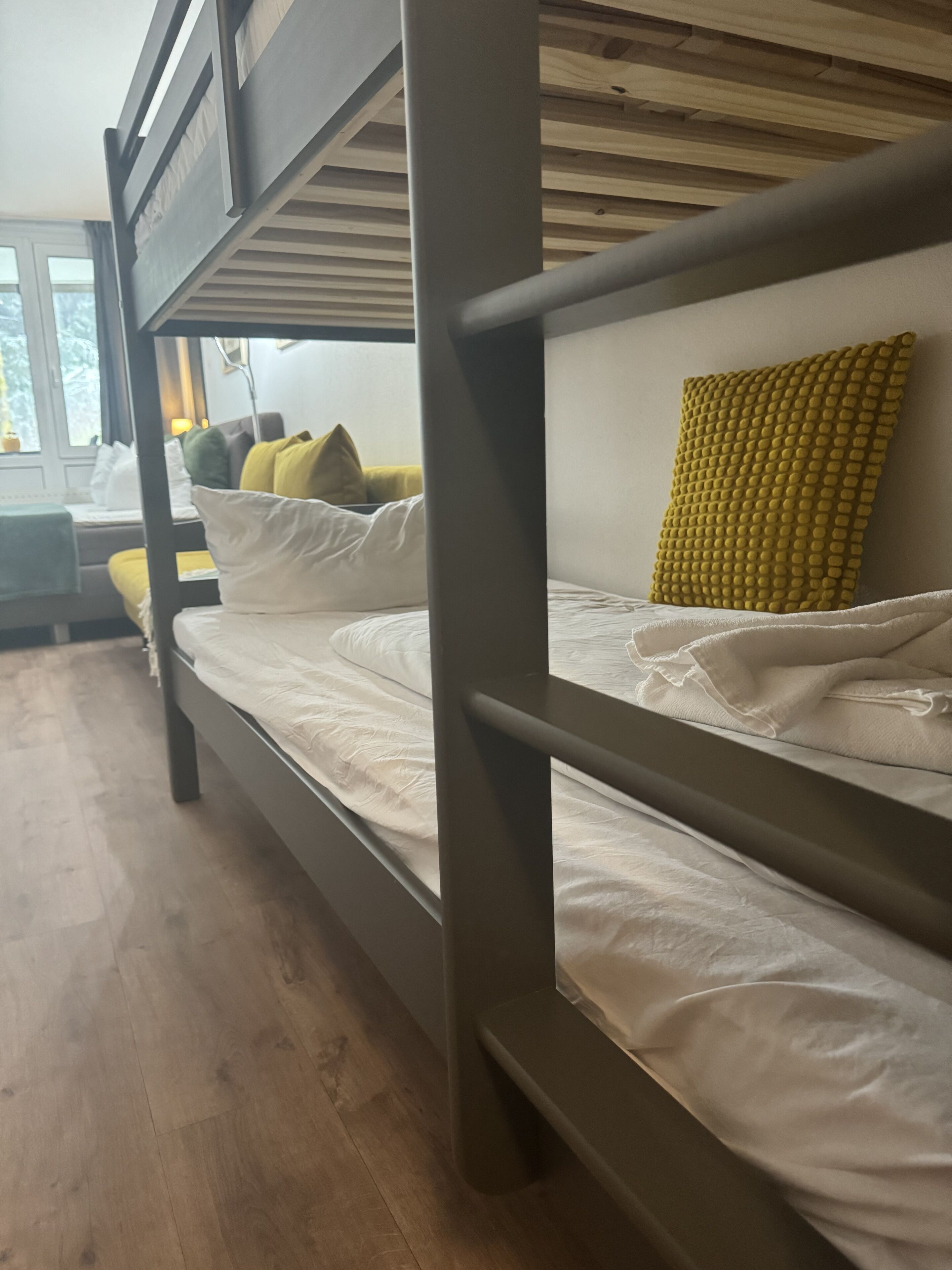Una cama litera con ropa de cama blanca y un cojín amarillo con textura.