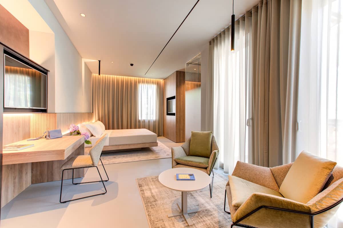 Una habitación de hotel moderna con un escritorio de madera, un sofá, una mesita redonda y un sillón cómodo.