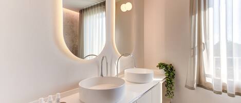 Un baño moderno con dos lavamanos redondos blancos, un espejo grande con iluminación integrada y una planta en maceta sobre la encimera.
