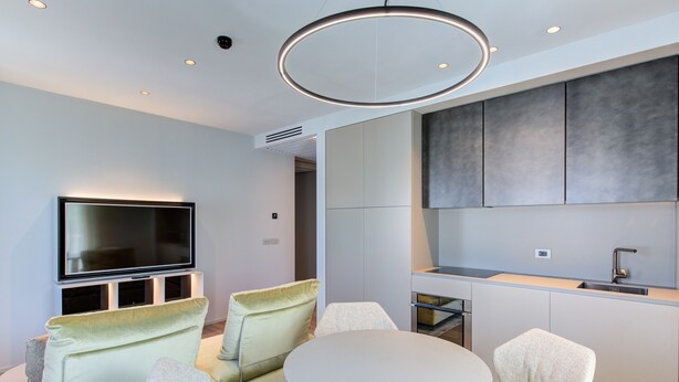 A modern living room with a flat-screen TV, two sofas, a round dining table, and a kitchen area with cabinets and a sink. - Villa Italia (Cesenatico)