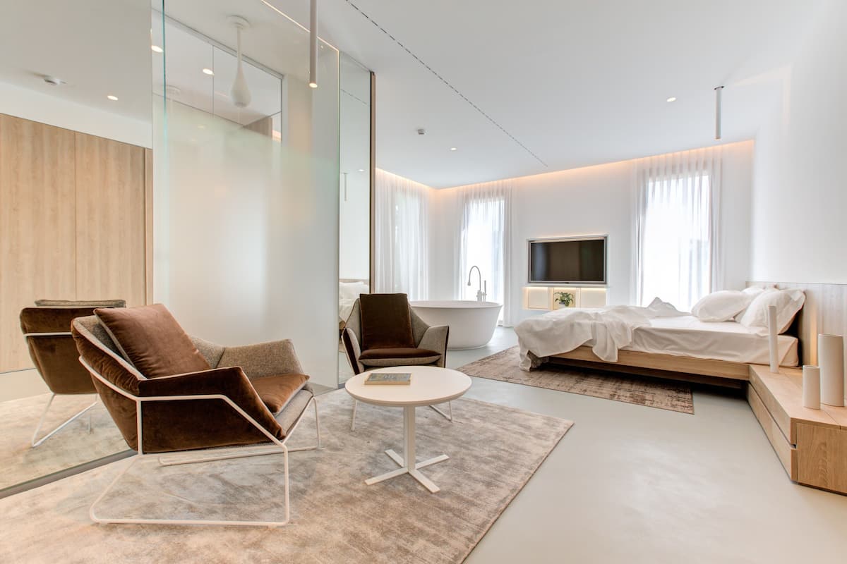 Una habitación de hotel moderna con sofá, sillón, mesa redonda y cama con televisión.