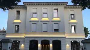 Un edificio imponente con una entrada monumental, múltiples ventanas con contraventanas y una fachada simétrica.