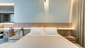 A modern hotel room with a large bed, a desk with a chair, a flat-screen TV, and a bedside table with two vases of flowers.
