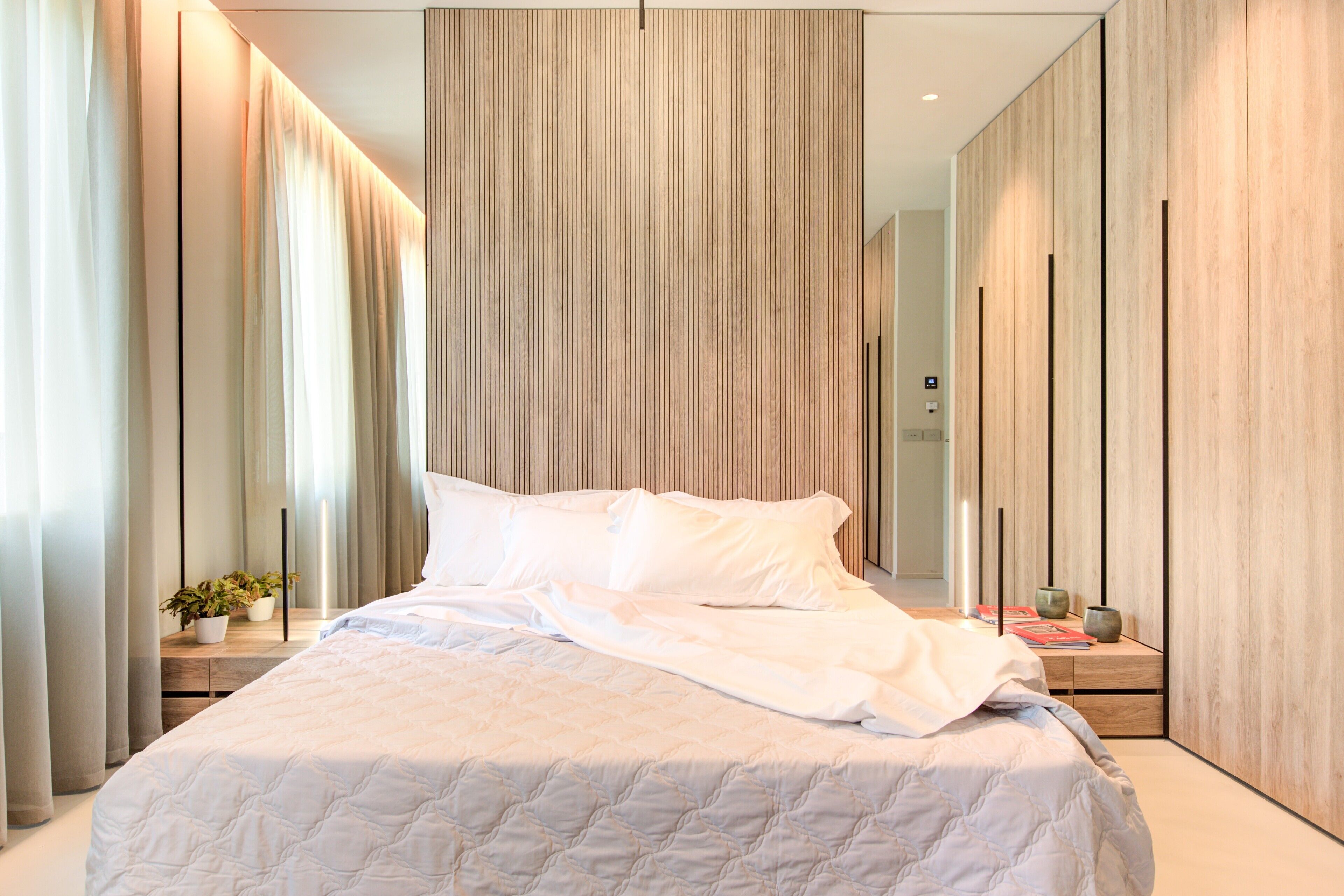Un dormitorio moderno con una cama grande, una mesita de noche con una planta y un espejo.