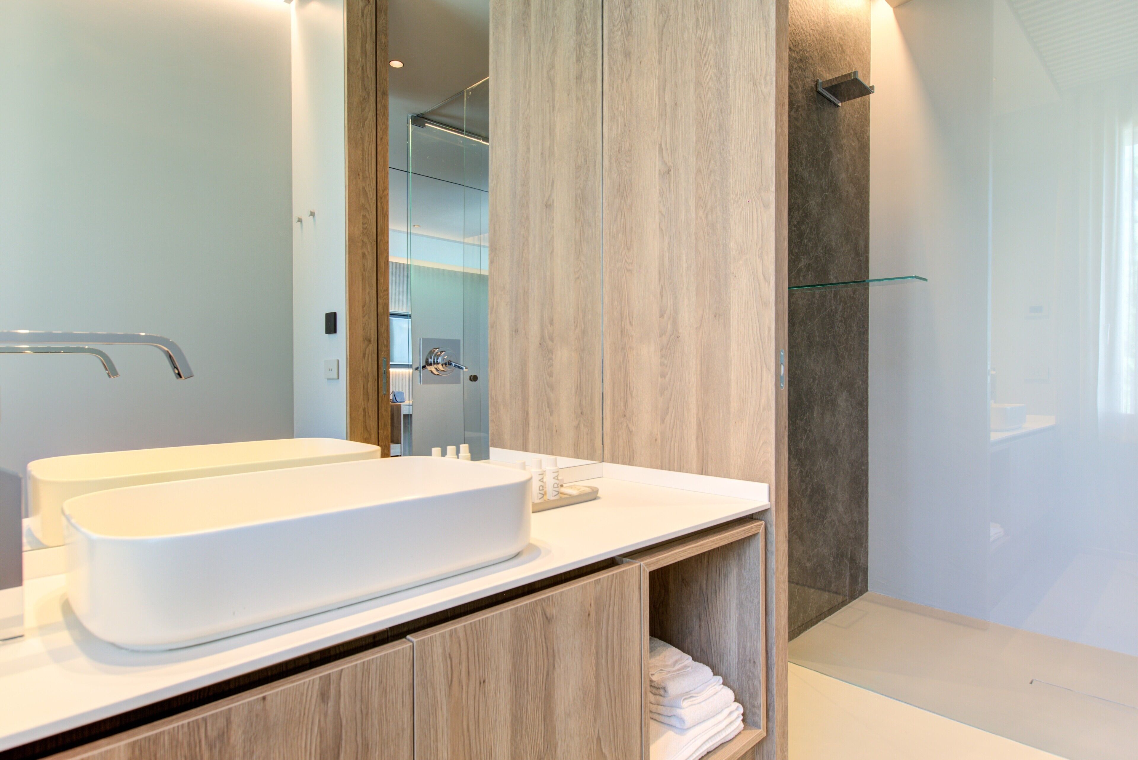 A modern bathroom with a large white sink, wooden cabinets, and a glass shower enclosure.