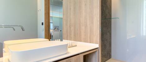 Ein modernes Badezimmer mit einem großen, weißen Waschbecken, Holzschränken und einer Glasdusche.