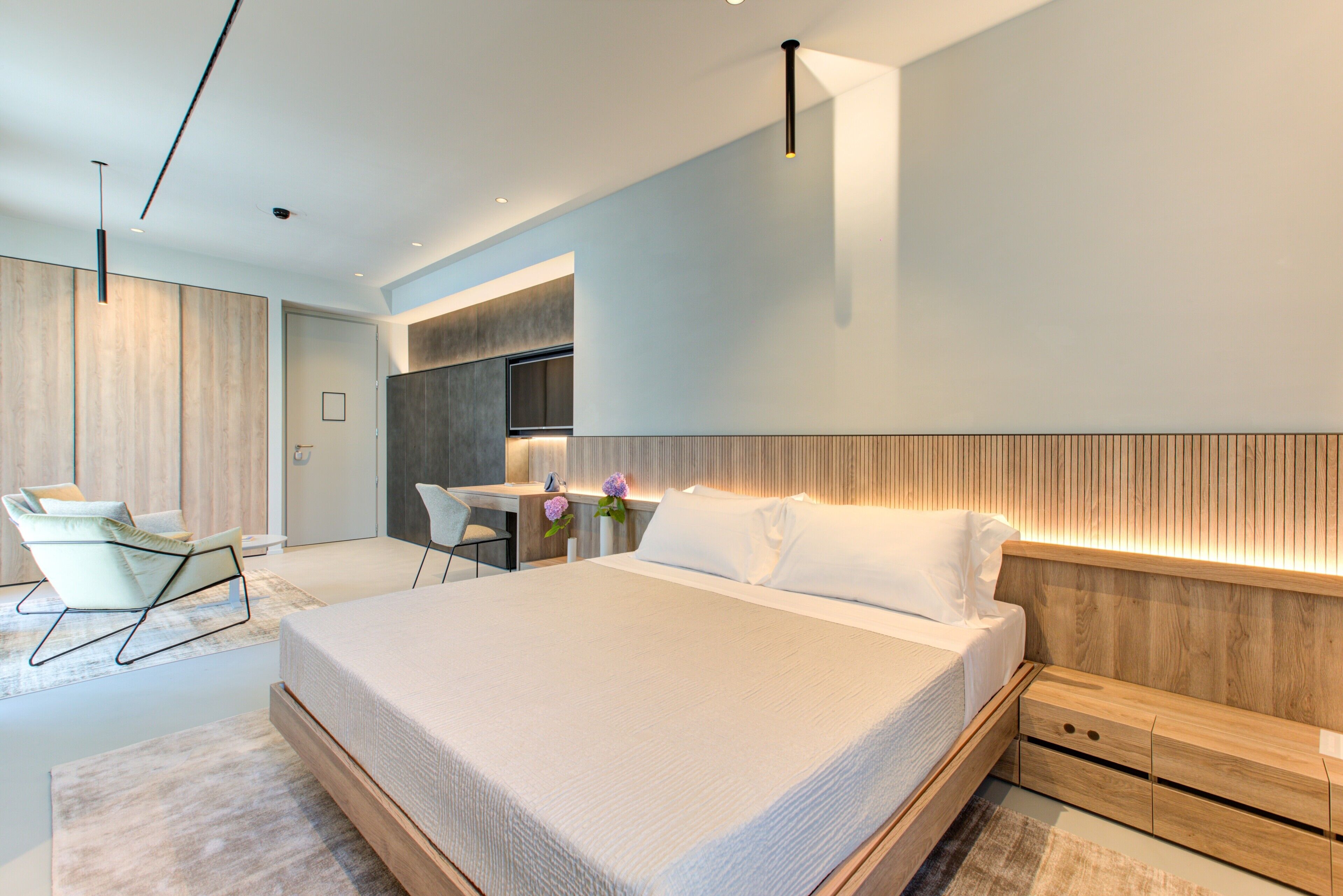 A modern bedroom with a large bed, a desk, and a chair.