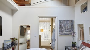A bedroom with a bed, a bedside table, a mirror, a bookshelf, and a door leading to a bathroom.