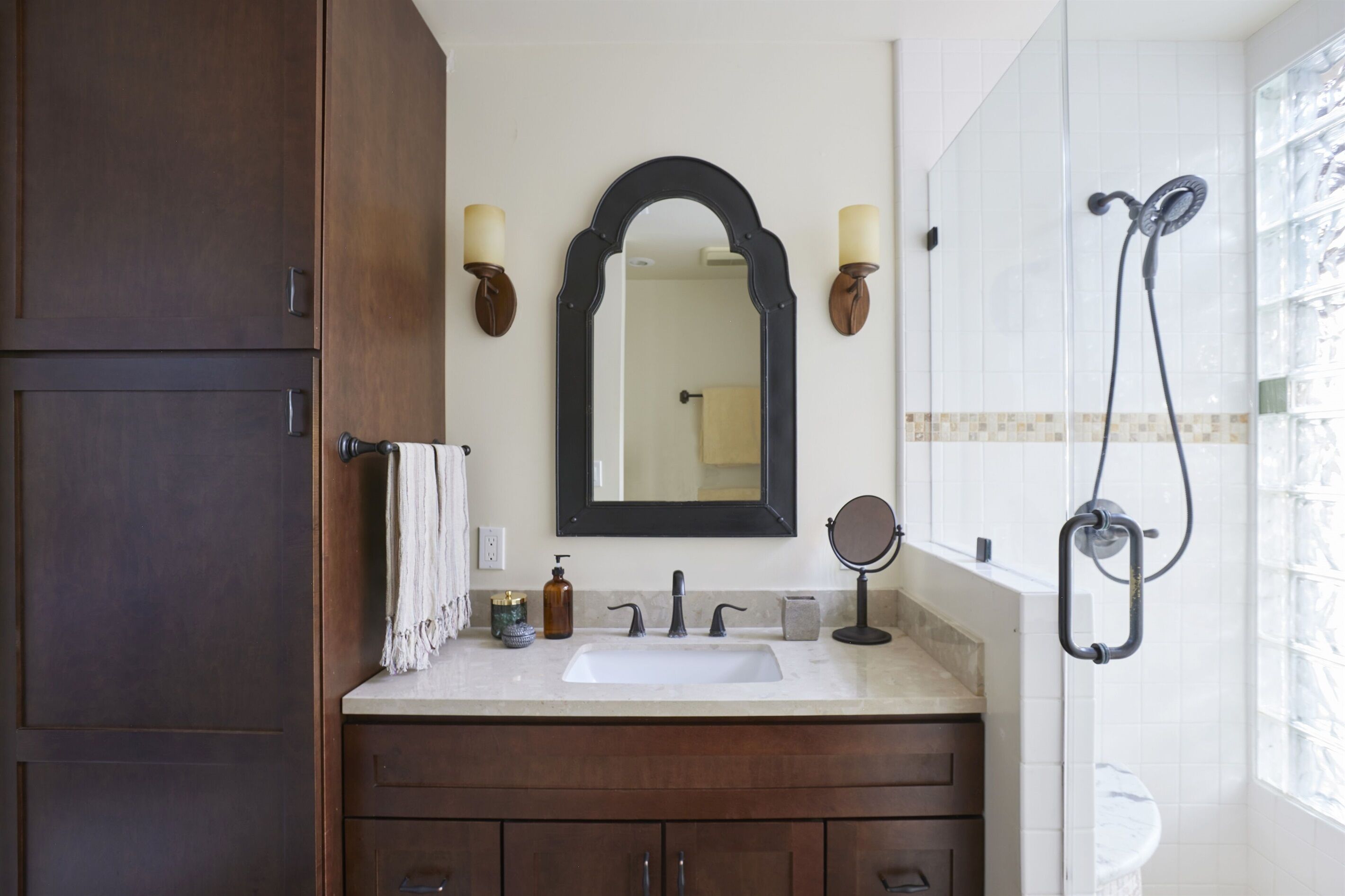 Un baño con un espejo grande, dos luces empotradas, un lavabo, un espejo de mano y una ducha con cabezal de ducha manual.