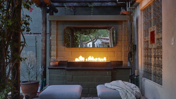 A cozy outdoor seating area with a fire feature, a mirror, and potted plants.