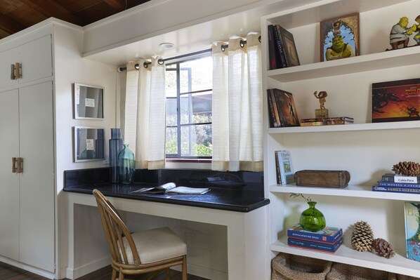 A kitchen with a wooden chair, a window with curtains, and a bookshelf with various items.