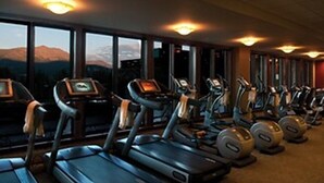 Una palestra con tapis roulant ed ellittiche disposte in file, ampie finestre con vista sulle montagne e luci a soffitto.