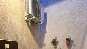 Een kleine badkamer met een witte wastafel, een wandairconditioner en drie potplanten.