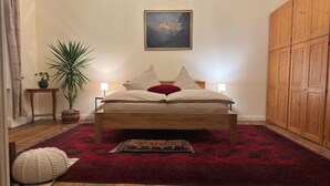A bedroom with a wooden bed, a red rug, a potted plant, and a wooden wardrobe. - Wohnung in Historischem Herrenhaus (Rhodt unter Rietburg)