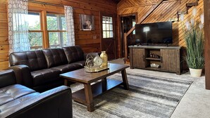 L’intérieur d’un chalet accueillant, avec un canapé en cuir, une table basse en bois et un téléviseur posé sur un meuble en bois.
