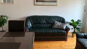 A living room with a dark green leather sofa, a wooden coffee table, and a framed painting on the wall.