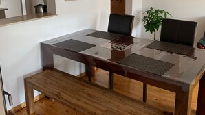 A dining area with a glass-top table, wooden benches, and chairs. There are wooden shelves and a mirror on the wall.