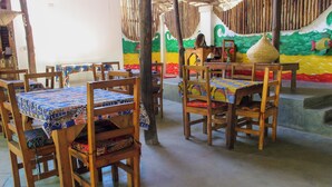 A restaurant with wooden tables and chairs, a colorful mural on the wall, and a woven basket on one table. - sagandobungalows (Michamvi)
