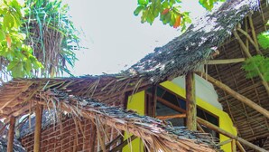 A wooden structure with a thatched roof, a staircase, and a red and yellow building in the background. - sagandobungalows (Michamvi)