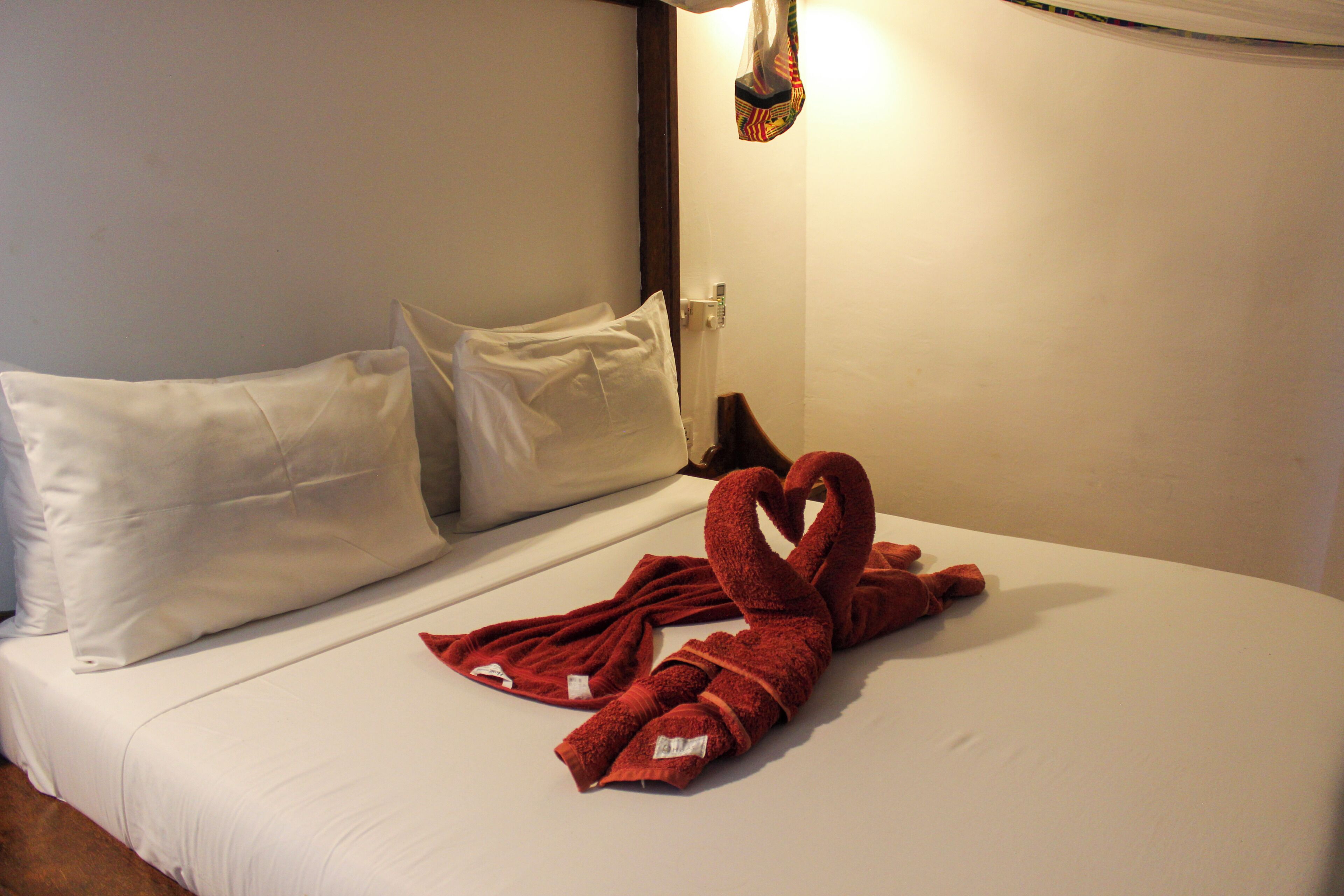Ein Hotelzimmer mit einem ordentlich bezogenem Bett, Kissen und einem Handtuch, das zu einem Herzen geformt ist.