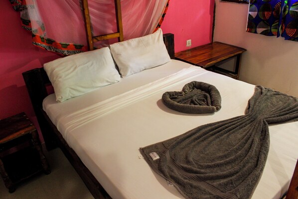 A bed with white linens, a gray towel, and a wooden nightstand beside it. - sagandobungalows (Michamvi)