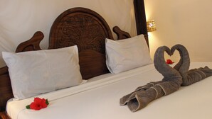 A neatly made bed with a heart-shaped towel arrangement and a single red flower on the pillow. - sagandobungalows (Michamvi)