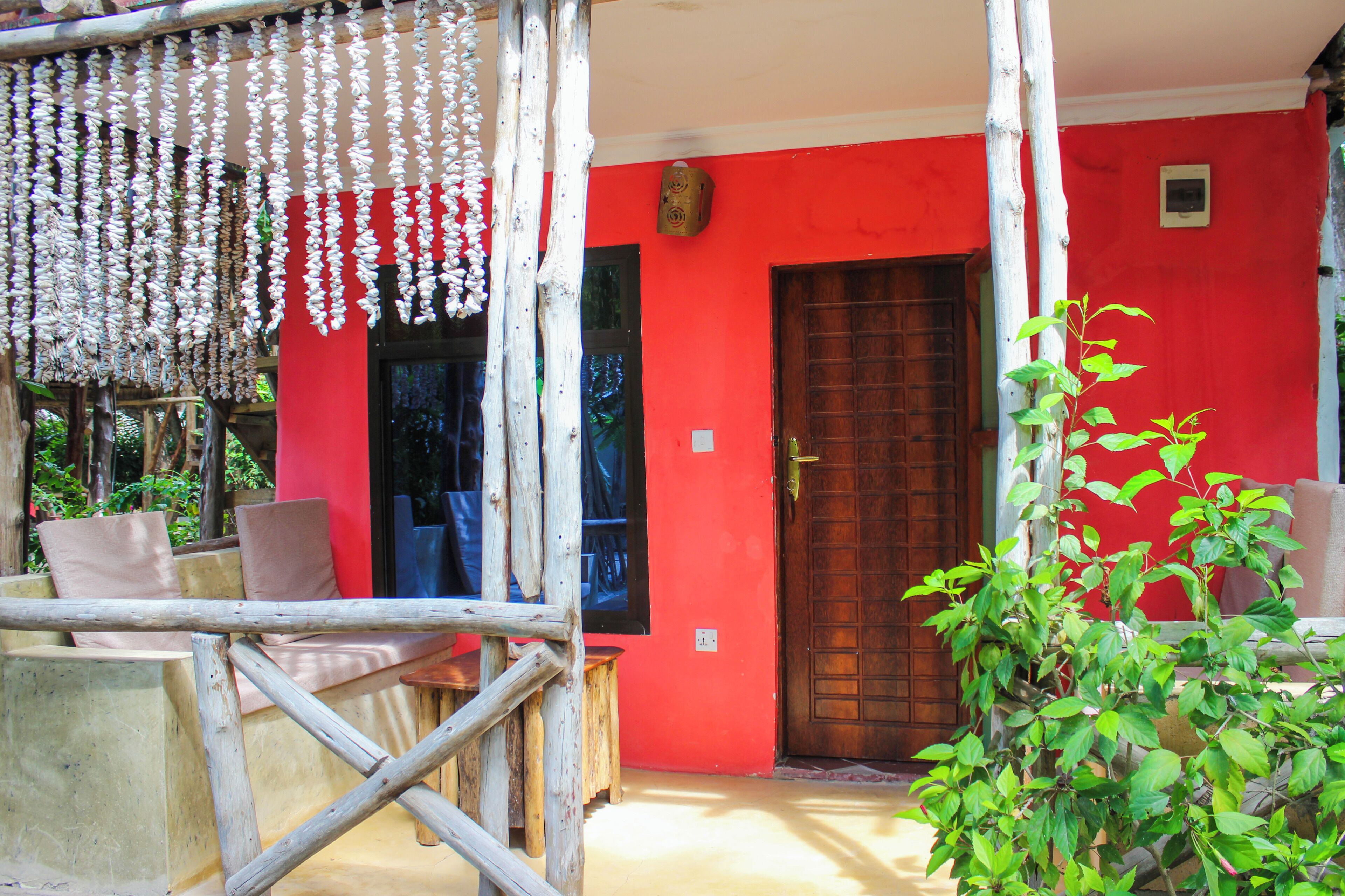 A red building with a wooden door, a balcony with chairs, and hanging decorations.