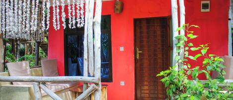A red building with a wooden door, a balcony with chairs, and hanging decorations.