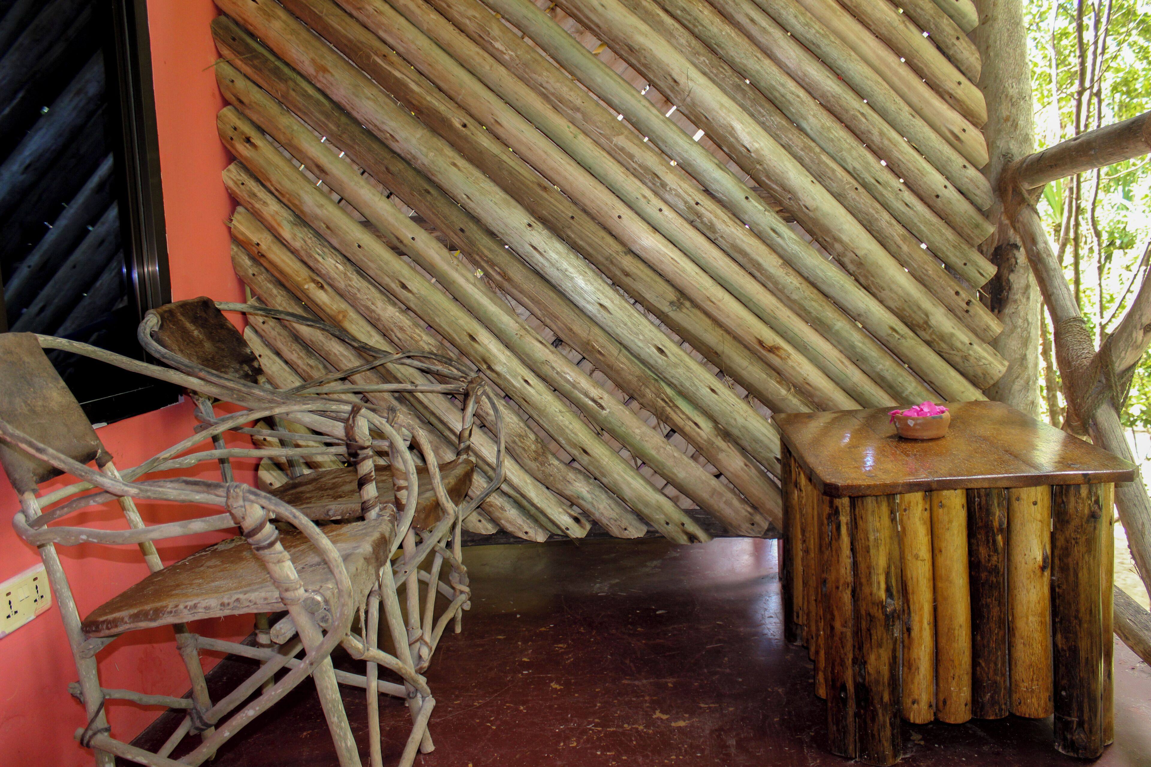 A rustic wooden chair and a small wooden table with a bowl on it, set against a backdrop of vertical wooden slats.