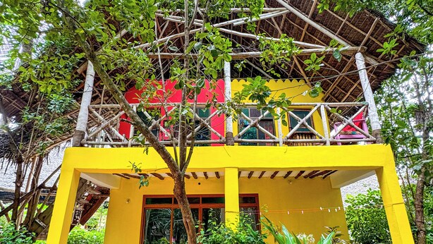 A two-story building with a yellow facade, a balcony, and a tree in the foreground. - sagandobungalows (Michamvi)