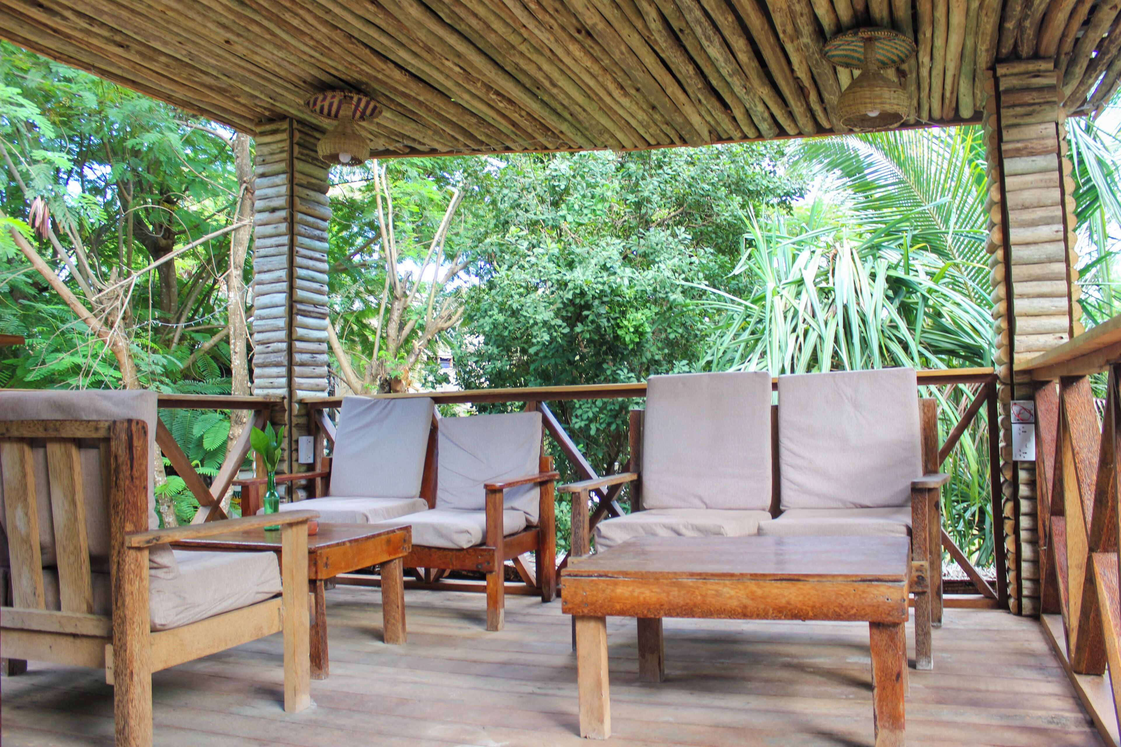 A wooden deck with chairs and a table, surrounded by lush greenery.