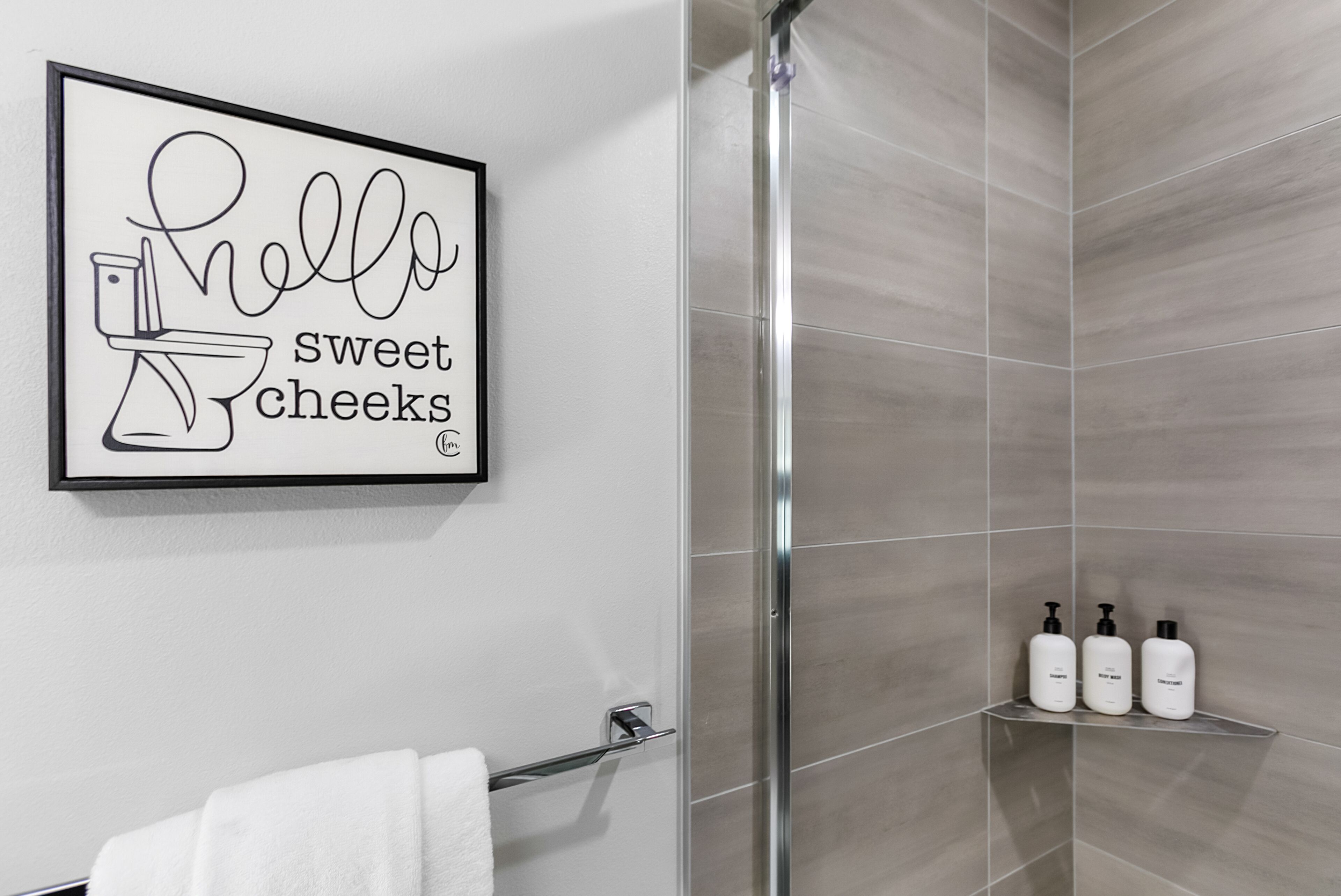 A modern bathroom with a shower, a framed sign, and a shelf with toiletries.